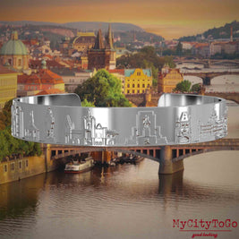 Versilberter Armreif mit Reliefs bekannter Sehenswürdigkeiten der Stadt Prag. Den Hintergrund bildet eine Ansicht der Stadt Prag.