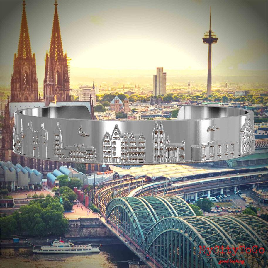 Versilberter Armreif mit Reliefs bekannter Sehenswürdigkeiten der Stadt Köln. Den Hintergrund bildet eine Ansicht der Stadt Koeln.