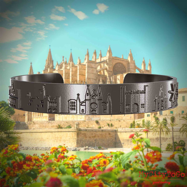 Armreif aus Titan mit Reliefs bekannter Sehenswürdigkeiten der Stadt Palma de Mallorca. Den Hintergrund bildet eine Ansicht der Stadt Palma de Mallorca.