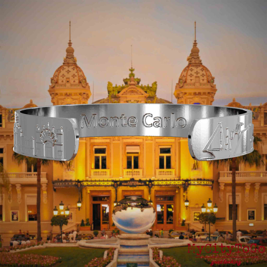 Innenseite eines silbernen Armreifs mit Reliefs bekannter Sehenswürdigkeiten der Stadt Monte Carlo und einer Gravur des Stadtnamens. Den Hintergrund bildet eine Ansicht der Stadt Monte Carlo.