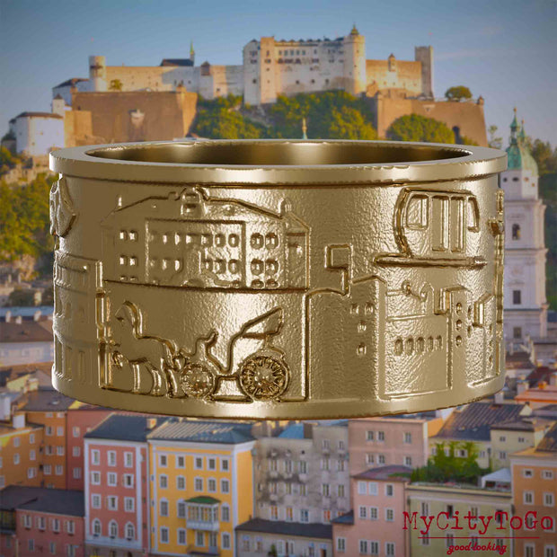 Ring aus vergoldetem Edelstahl mit Reliefs bekannter Sehenswürdigkeiten der Stadt Salzburg. Den Hintergrund bildet eine Ansicht der Stadt Salzburg.