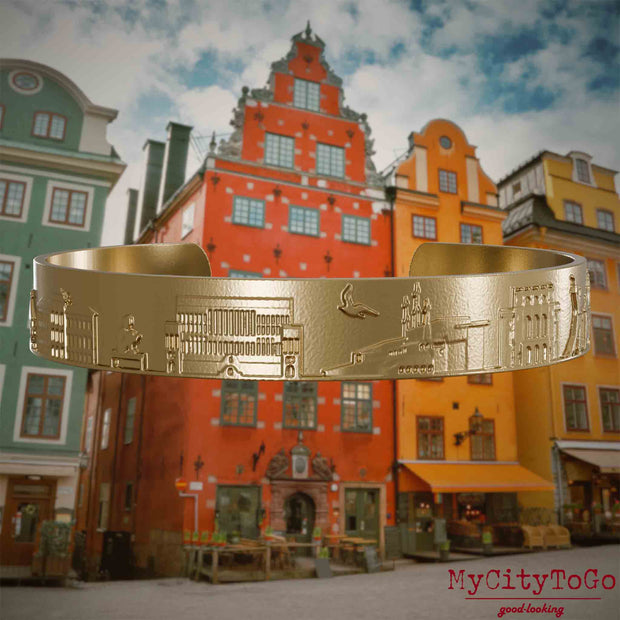 Armreif aus vergoldetem Edelstahl mit Reliefs bekannter Sehenswürdigkeiten der Stadt Stockholm. Den Hintergrund bildet eine Ansicht der Stadt Stockholm.