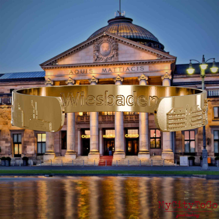 Inside of a gold-plated bangle featuring reliefs of well-known landmarks in the city of Wiesbaden and an engraving of the city’s name. The background is a view of the city of Wiesbaden.