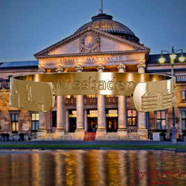 Inside of a gold-plated bangle featuring reliefs of well-known landmarks in the city of Wiesbaden and an engraving of the city’s name. The background is a view of the city of Wiesbaden.