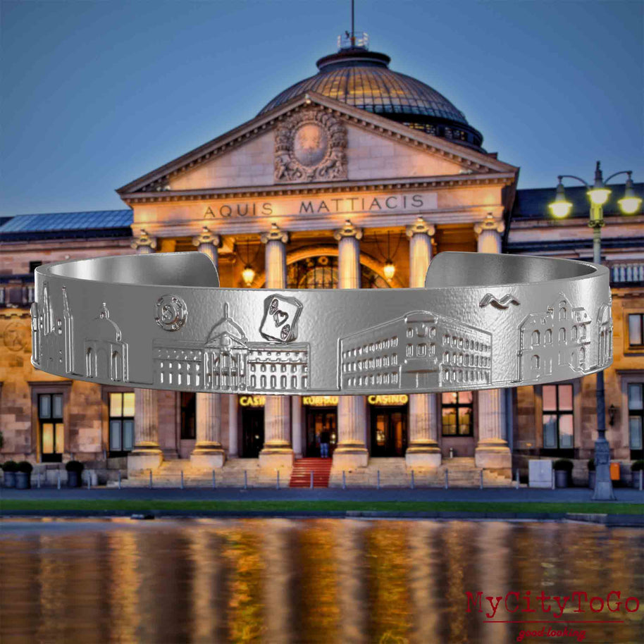 Bangle made of stainless steel with reliefs of well-known landmarks of the city of Wiesbaden. The background features a view of the city of Wiesbaden.