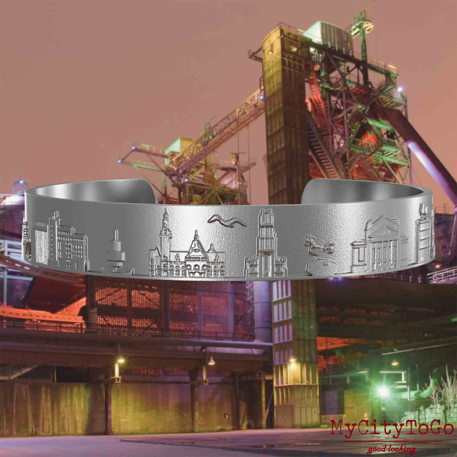 Bangle made of stainless steel with reliefs of well-known landmarks of the city of Duisburg. The background features a view of the city of Duisburg.