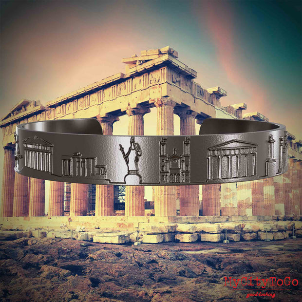 Armreif aus Titan mit Reliefs bekannter Sehenswürdigkeiten der Stadt Athen. Den Hintergrund bildet eine Ansicht der Stadt Athen.