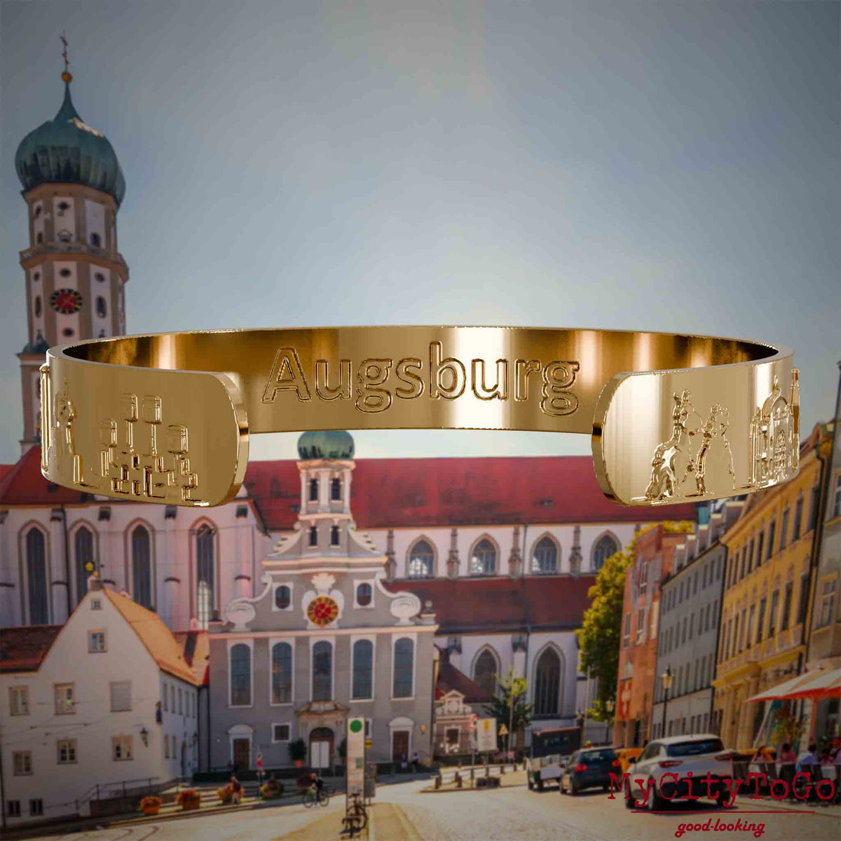Innenseite eines vergoldeten Armreifs mit Reliefs bekannter Sehenswürdigkeiten der Stadt Augsburg und einer Gravur des Stadtnamens . Den Hintergrund bildet eine Ansicht der Stadt Augsburg.