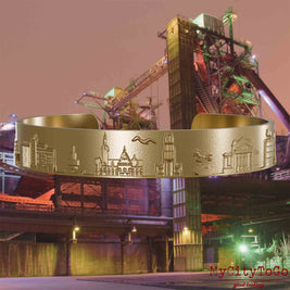 Bangle made of gold-plated stainless steel with reliefs of well-known landmarks of the city of Duisburg. The background features a view of the city of Duisburg.