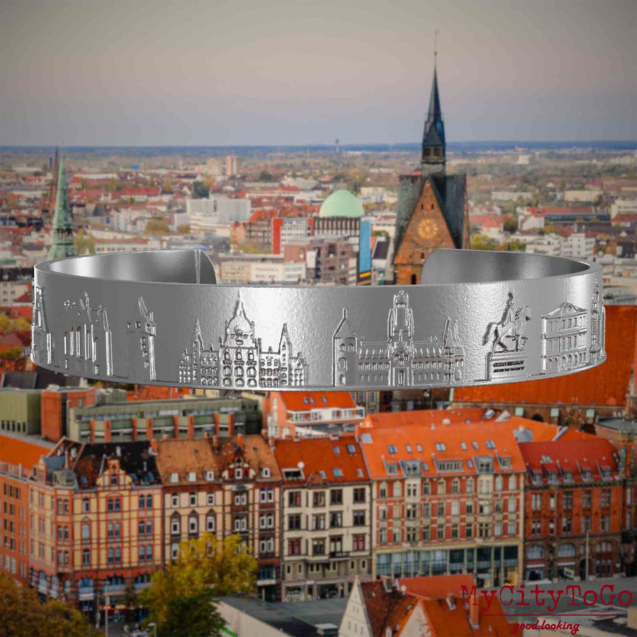 Armreif aus Edelstahl mit Reliefs bekannter Sehenswürdigkeiten der Stadt Hannover. Den Hintergrund bildet eine Ansicht der Stadt Hannover.