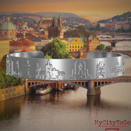 Armreif aus Edelstahl mit Reliefs bekannter Sehenswürdigkeiten der Stadt Prag. Den Hintergrund bildet eine Ansicht der Stadt Prag.