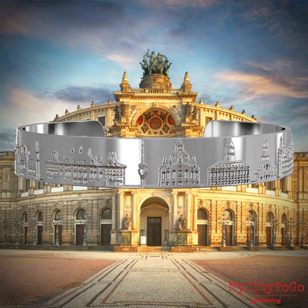 Silberner Armreif mit Reliefs bekannter Sehenswürdigkeiten der Stadt Dresden. Den Hintergrund bildet eine Ansicht der Stadt Dresden.