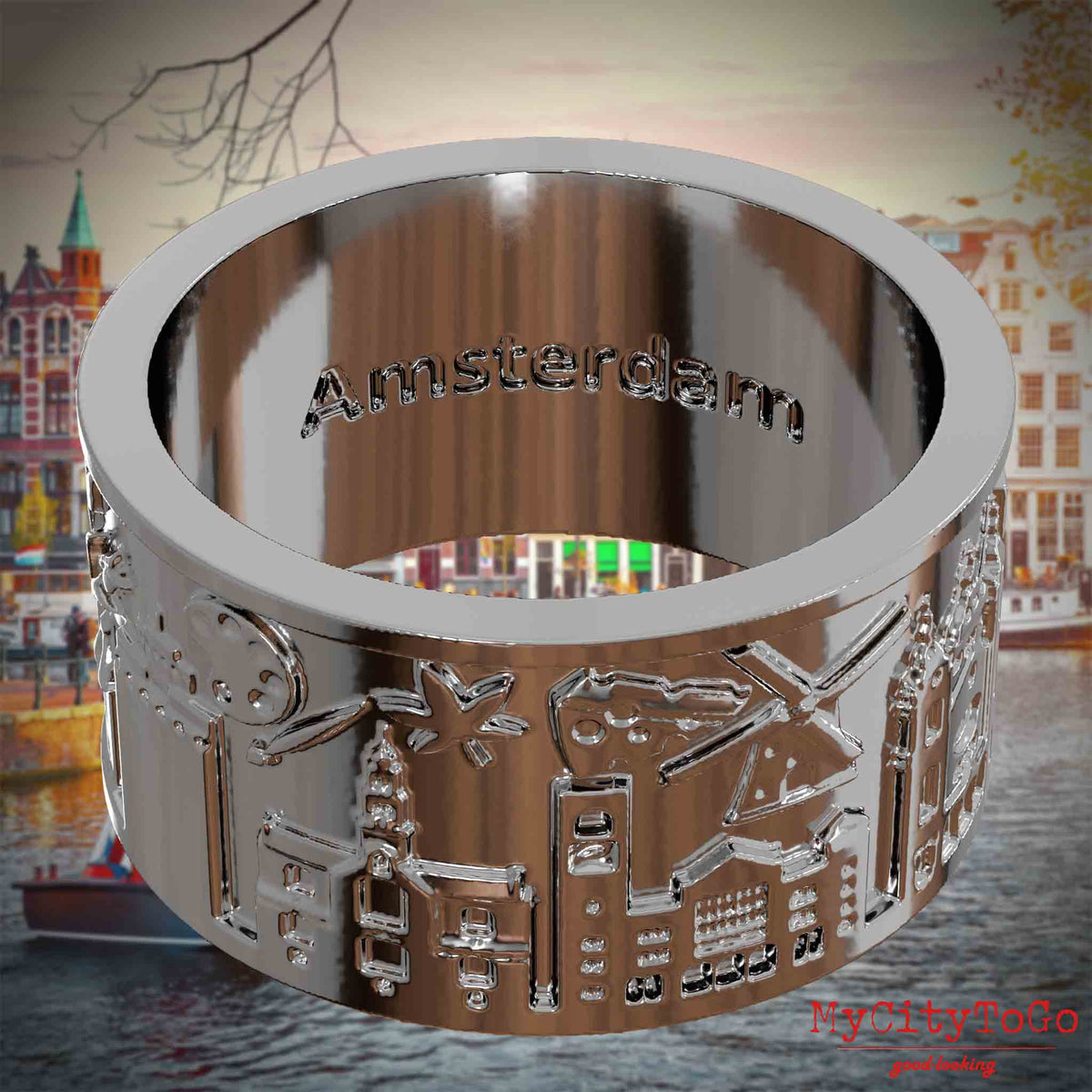 Versilberter Ring mit Reliefs bekannter Sehenswürdigkeiten der Stadt Amsterdam und einer Gravur des Stadtnamens auf der Innenseite. Den Hintergrund bildet eine Ansicht der Stadt Amsterdam.
