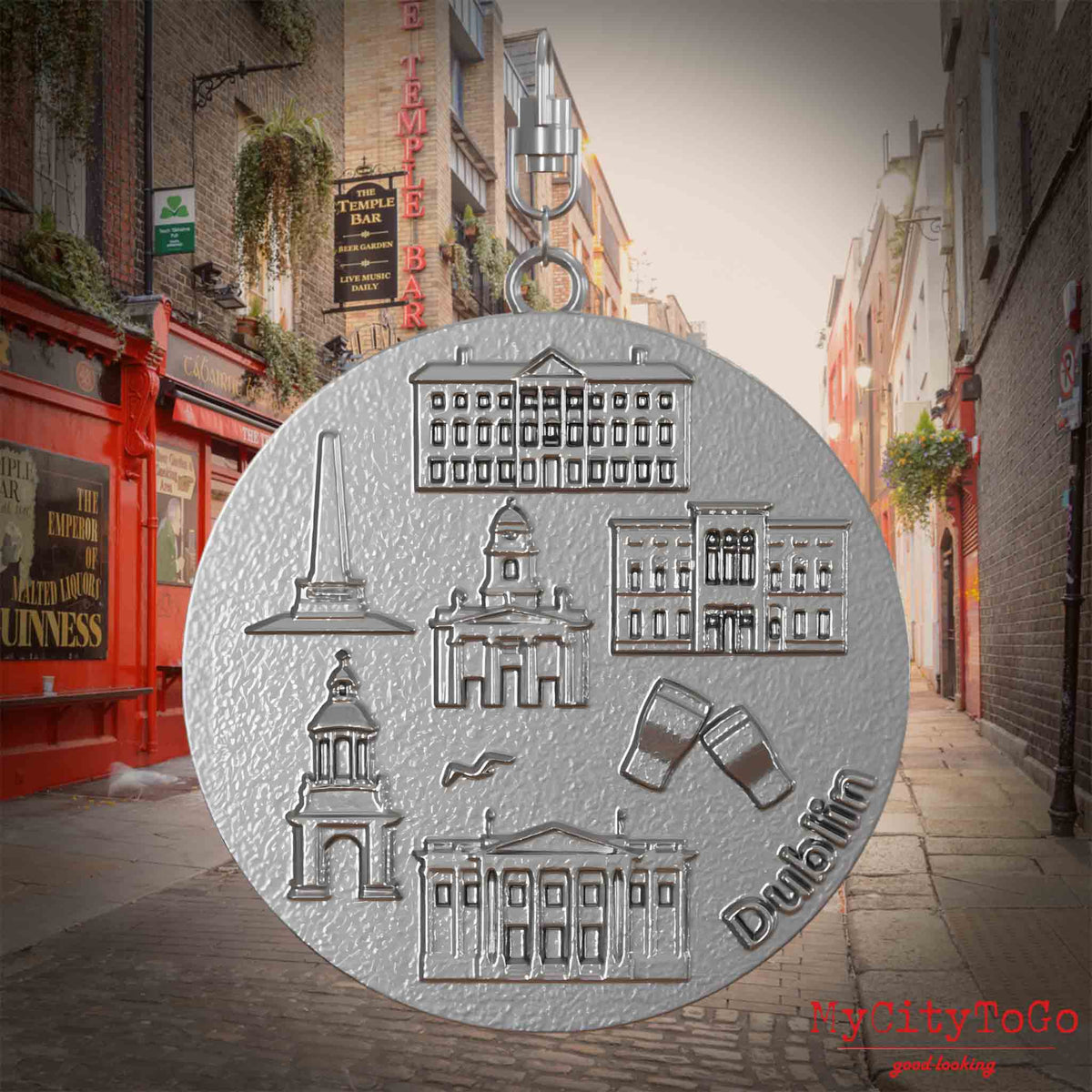 Halskette mit Drehwirbel und Vorderseite eines Schmuckanhängers aus Edelstahl, auf dem Reliefs bekannter Sehenswürdigkeiten der Stadt Dublin abgebildet sind. Den Hintergrund bildet eine Ansicht der Stadt Dublin.
