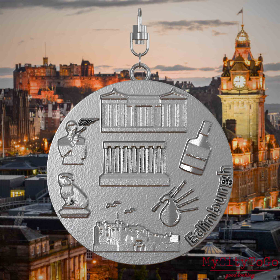 Halskette mit Drehwirbel und Vorderseite eines Schmuckanhängers aus Edelstahl, auf dem Reliefs bekannter Sehenswürdigkeiten der Stadt Edinburgh abgebildet sind. Den Hintergrund bildet eine Ansicht der Stadt Edinburgh.
