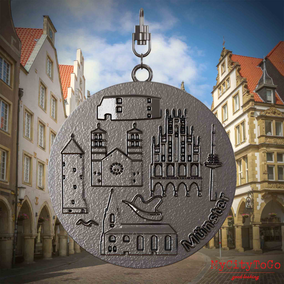 Halskette mit Drehwirbel und Vorderseite eines Schmuckanhängers aus Titan, auf dem Reliefs bekannter Sehenswürdigkeiten der Stadt Muenster abgebildet sind. Den Hintergrund bildet eine Ansicht der Stadt Muenster.