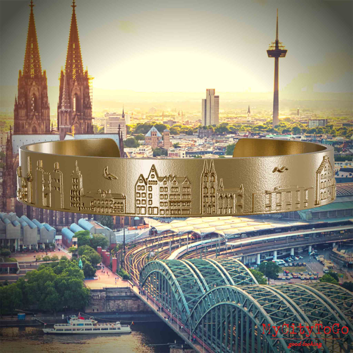 Armreif aus vergoldetem Edelstahl mit Reliefs bekannter Sehenswürdigkeiten der Stadt Köln. Den Hintergrund bildet eine Ansicht der Stadt Koeln.