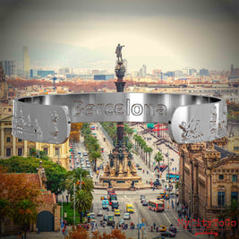 Innenseite eines silbernen Armreifs mit Reliefs bekannter Sehenswürdigkeiten der Stadt Barcelona und einer Gravur des Stadtnamens. Den Hintergrund bildet eine Ansicht der Stadt Barcelona.