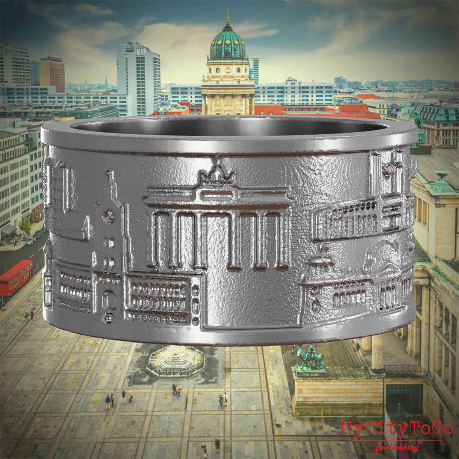 Ring aus Edelstahl mit Reliefs bekannter Sehenswürdigkeiten der Stadt Berlin. Den Hintergrund bildet eine Ansicht der Stadt Berlin. 
