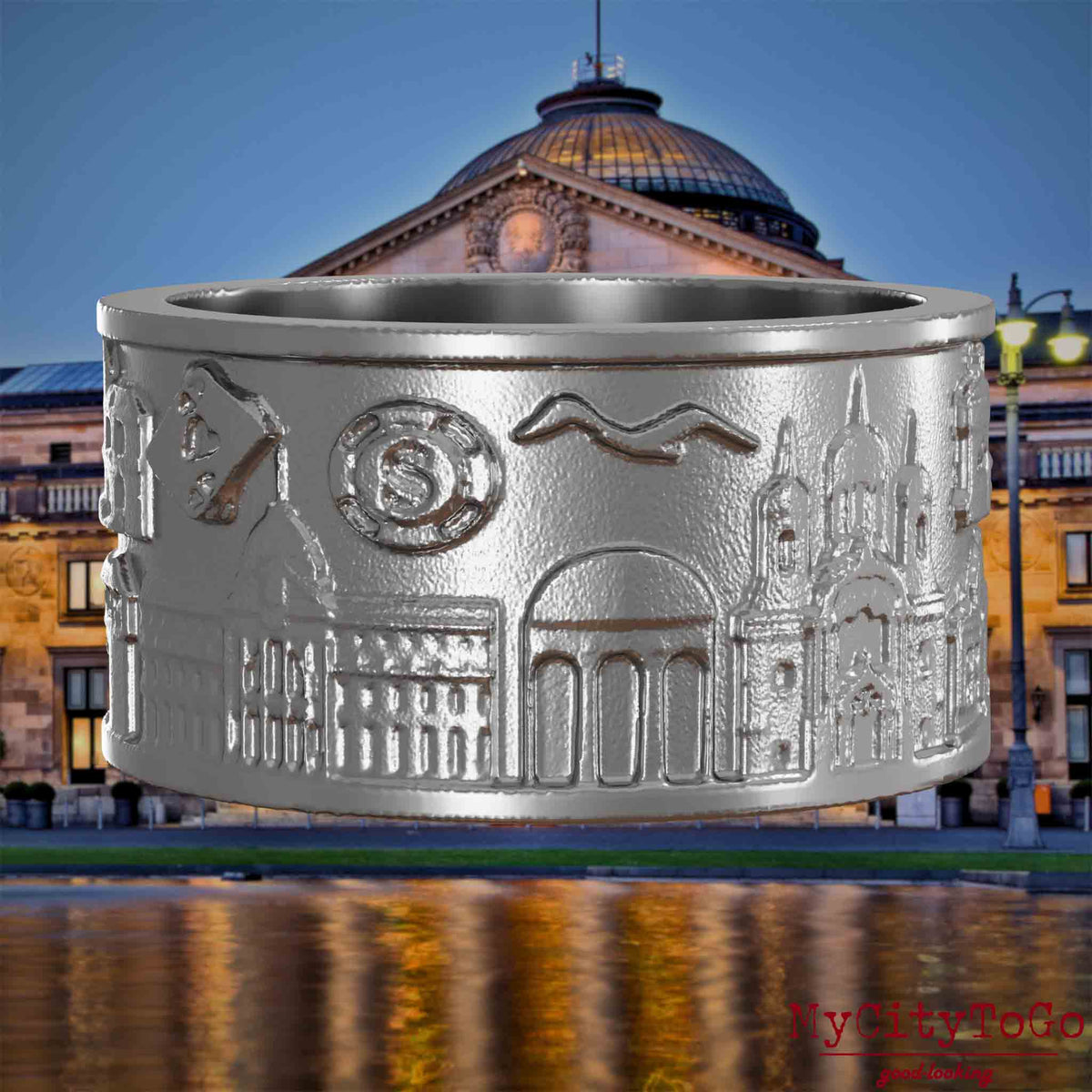Ring aus Edelstahl mit Reliefs bekannter Sehenswürdigkeiten der Stadt Wiesbaden.  Den Hintergrund bildet eine Ansicht der Stadt Wiesbaden.