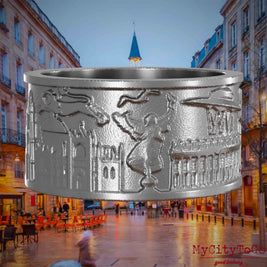 Ring aus Edelstahl mit Reliefs bekannter Sehenswürdigkeiten der Stadt Bordeaux. Den Hintergrund bildet eine Ansicht der Stadt Bordeaux.