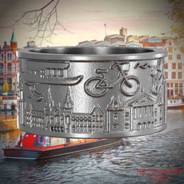 Ring aus Edelstahl mit Reliefs bekannter Sehenswürdigkeiten der Stadt Amsterdam. Den Hintergrund bildet eine Ansicht der Stadt Amsterdam.