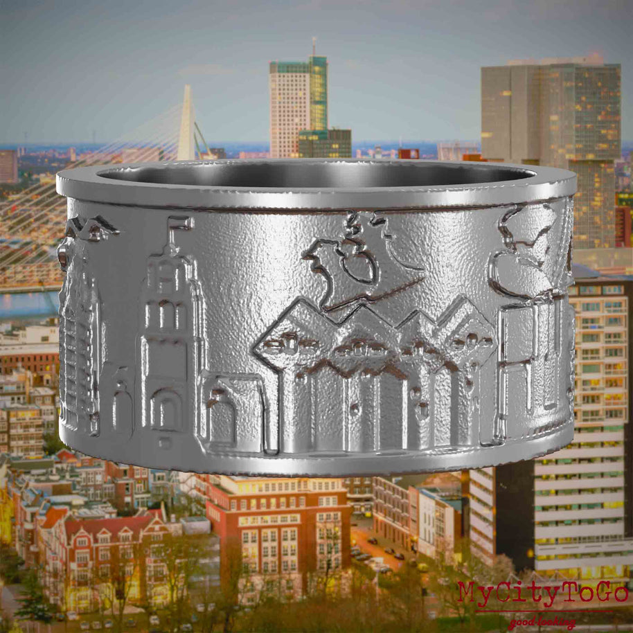 Ring aus Edelstahl mit Reliefs bekannter Sehenswürdigkeiten der Stadt Rotterdam. Den Hintergrund bildet eine Ansicht der Stadt Rotterdam.