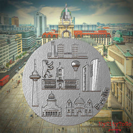 Halskette mit Drehwirbel und Vorderseite eines Schmuckanhängers aus Edelstahl, auf dem Reliefs bekannter Sehenswürdigkeiten der Stadt Berlin abgebildet sind. Den Hintergrund bildet eine Ansicht der Stadt Berlin.