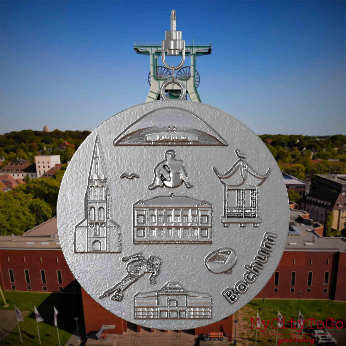 Halskette mit Drehwirbel und Vorderseite eines Schmuckanhängers aus Edelstahl, auf dem Reliefs bekannter Sehenswürdigkeiten der Stadt Bochum abgebildet sind. Den Hintergrund bildet eine Ansicht der Stadt Bochum .
