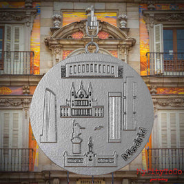Halskette mit Drehwirbel und Rückseite eines Schmuckanhängers aus Edelstahl, auf dem Reliefs bekannter Sehenswürdigkeiten der Stadt Madrid abgebildet sind. Den Hintergrund bildet eine Ansicht der Stadt Madrid.
