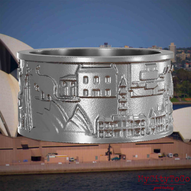 Ring aus Edelstahl mit Reliefs bekannter Sehenswürdigkeiten der Stadt Sydney. Den Hintergrund bildet eine Ansicht der Stadt Sydney.