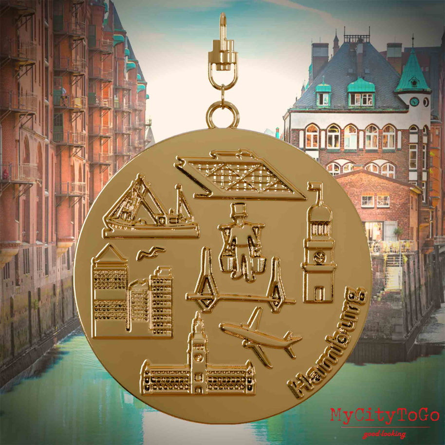 Halskette mit Drehwirbel und Vorderseite eines vergoldeten Schmuckanhängers, auf dem Reliefs bekannter Sehenswürdigkeiten der Stadt Hamburg abgebildet sind. Den Hintergrund bildet eine Ansicht der Stadt Hamburg.