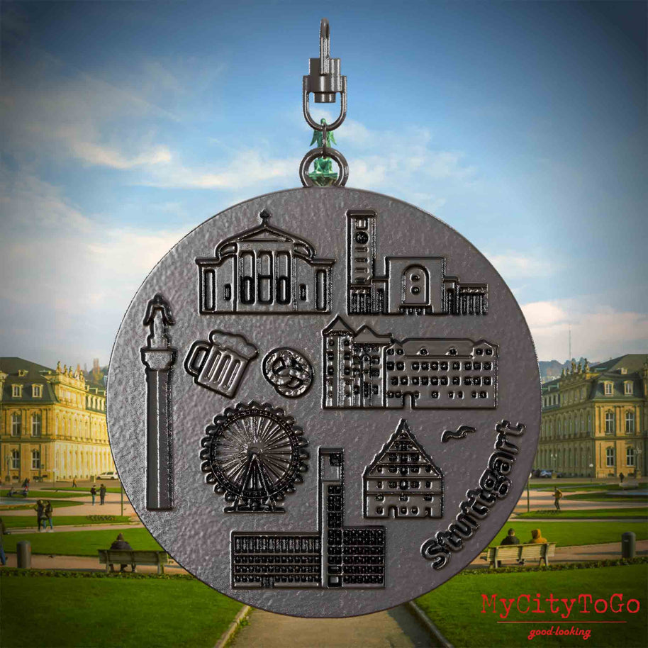 Halskette mit Drehwirbel und Rückseite eines Schmuckanhängers aus Titan, auf dem Reliefs bekannter Sehenswürdigkeiten der Stadt Stuttgart abgebildet sind. Den Hintergrund bildet eine Ansicht der Stadt Stuttgart.
