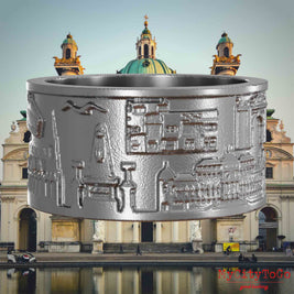 Ring aus Edelstahl mit Reliefs bekannter Sehenswürdigkeiten der Stadt Wien. Den Hintergrund bildet eine Ansicht der Stadt Wien.