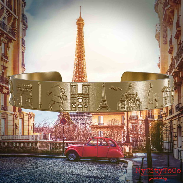 Armreif aus vergoldetem Edelstahl mit Reliefs bekannter Sehenswürdigkeiten der Stadt Paris. Den Hintergrund bildet eine Ansicht der Stadt Paris.