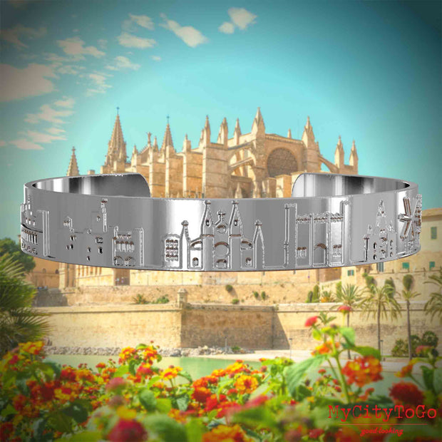 Versilberter Armreif mit Reliefs bekannter Sehenswürdigkeiten der Stadt Palma de Mallorca. Den Hintergrund bildet eine Ansicht der Stadt Palma de Mallorca.
