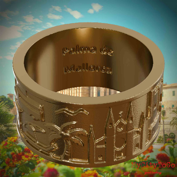 Ring aus vergoldetem Edelstahl mit Reliefs bekannter Sehenswürdigkeiten der Stadt Palma de Mallorca und einer Gravur des Stadtnamens auf der Innenseite. Den Hintergrund bildet eine Ansicht der Stadt Palma de Mallorca.