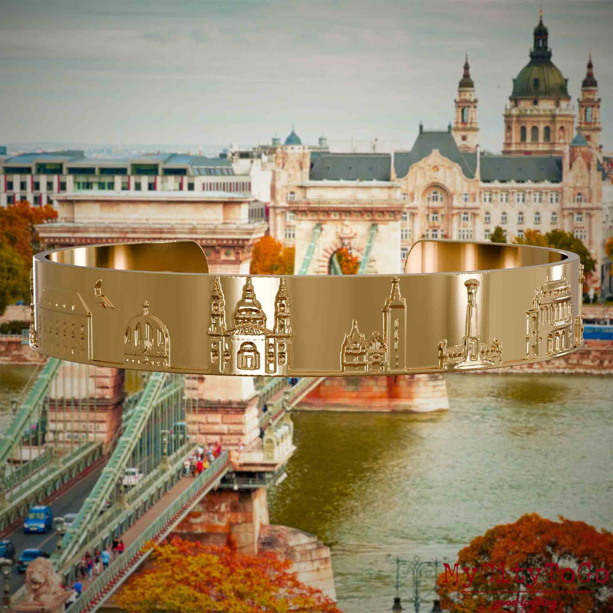 Vergoldeter Armreif mit Reliefs bekannter Sehenswürdigkeiten der Stadt Budapest. Den Hintergrund bildet eine Ansicht der Stadt Budapest.