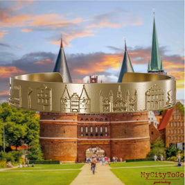 Armreif aus vergoldetem Edelstahl mit Reliefs bekannter Sehenswürdigkeiten der Stadt Luebeck. Den Hintergrund bildet eine Ansicht der Stadt Luebeck.