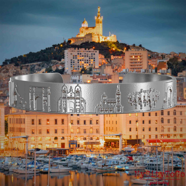Armreif aus Edelstahl mit Reliefs bekannter Sehenswürdigkeiten der Stadt Marseille. Den Hintergrund bildet eine Ansicht der Stadt Marseille.