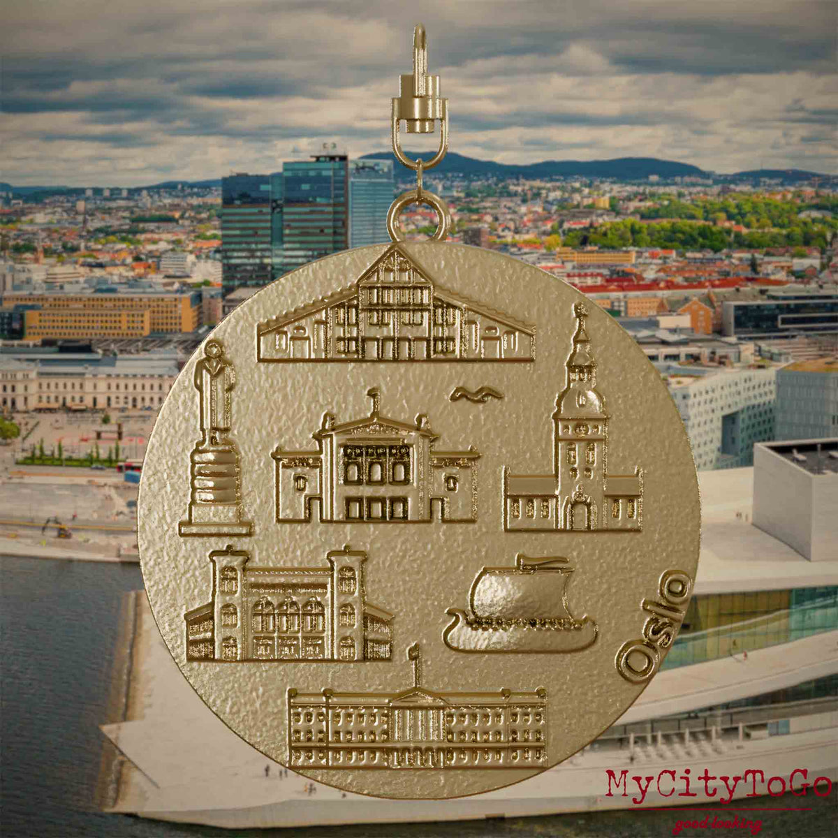 Halskette mit Drehwirbel und Rückseite eines Schmuckanhängers aus vergoldetem Edelstahl, auf dem Reliefs bekannter Sehenswürdigkeiten der Stadt Oslo abgebildet sind. Den Hintergrund bildet eine Ansicht der Stadt Oslo.
