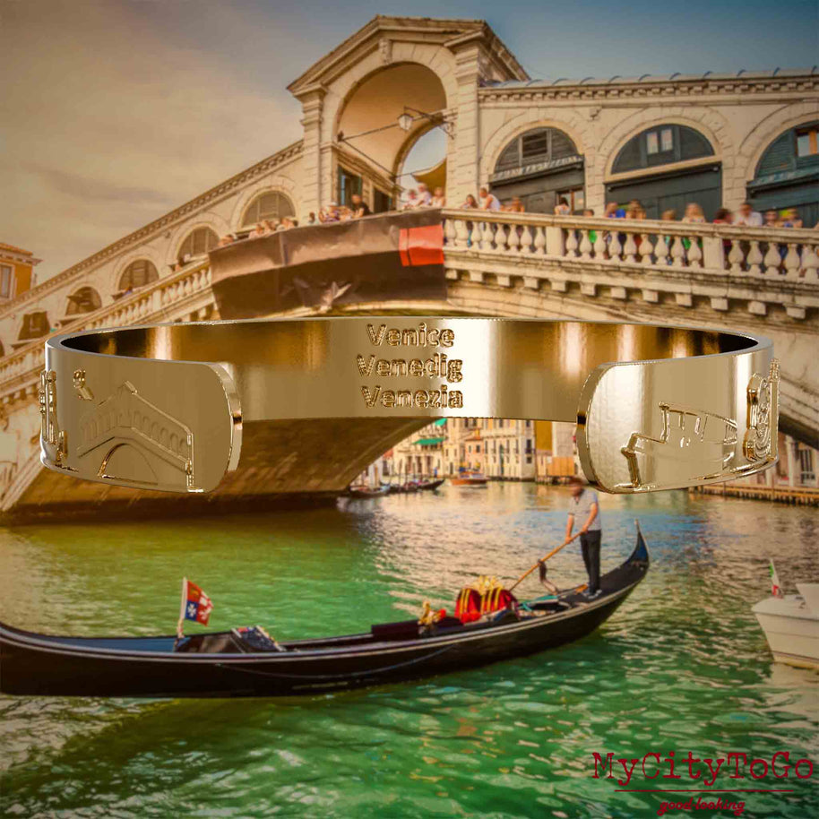 Innenseite eines vergoldeten Armreifs mit Reliefs bekannter Sehenswürdigkeiten der Stadt Venedig und einer Gravur des Stadtnamens. Den Hintergrund bildet eine Ansicht der Stadt Venedig.