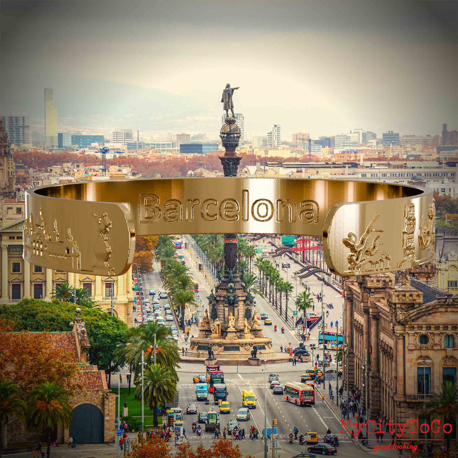 Innenseite eines vergoldeten Armreifs mit Reliefs bekannter Sehenswürdigkeiten der Stadt Barcelona und einer Gravur des Stadtnamens. Den Hintergrund bildet eine Ansicht der Stadt Barcelona.