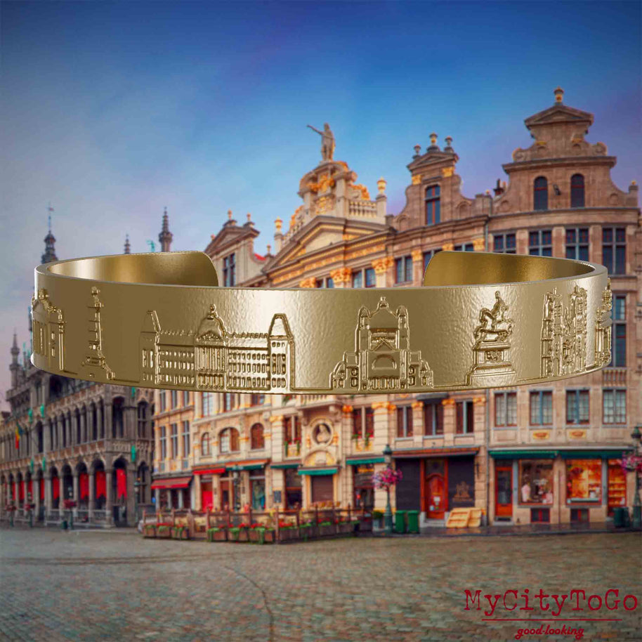 Armreif aus vergoldetem Edelstahl mit Reliefs bekannter Sehenswürdigkeiten der Stadt Brüssel. Den Hintergrund bildet eine Ansicht der Stadt Bruessel.