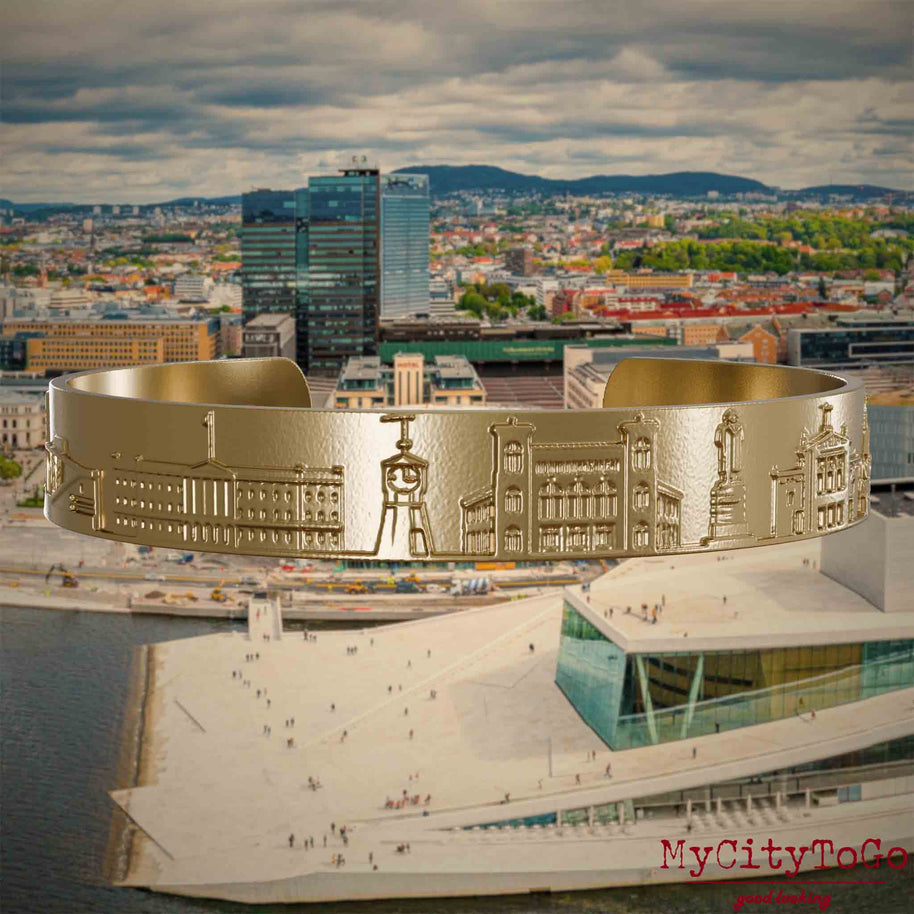 Armreif aus vergoldetem Edelstahl mit Reliefs bekannter Sehenswürdigkeiten der Stadt Oslo. Den Hintergrund bildet eine Ansicht der Stadt Oslo.