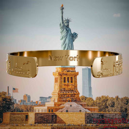 Innenseite eines vergoldeten Armreifs mit Reliefs bekannter Sehenswürdigkeiten der Stadt New York und einer Gravur des Stadtnamens. Den Hintergrund bildet eine Ansicht der Stadt New York.