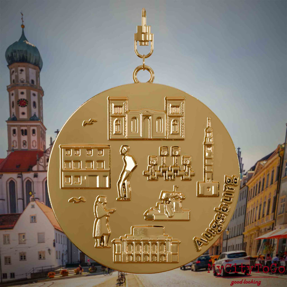 Halskette mit Drehwirbel und Vorderseite eines vergoldeten Schmuckanhängers, auf dem Reliefs bekannter Sehenswürdigkeiten der Stadt Augsburg abgebildet sind. Den Hintergrund bildet eine Ansicht der Stadt Augsburg .
