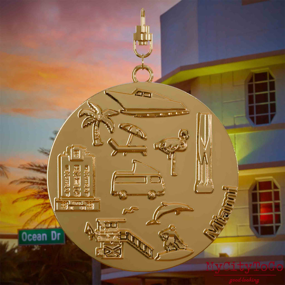 Halskette mit Drehwirbel und Rückseite eines vergoldeten Schmuckanhängers, auf dem Reliefs bekannter Sehenswürdigkeiten der Stadt Miami abgebildet sind. Den Hintergrund bildet eine Ansicht der Stadt Miami.
