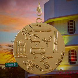 Halskette mit Drehwirbel und Rückseite eines vergoldeten Schmuckanhängers, auf dem Reliefs bekannter Sehenswürdigkeiten der Stadt Miami abgebildet sind. Den Hintergrund bildet eine Ansicht der Stadt Miami.
