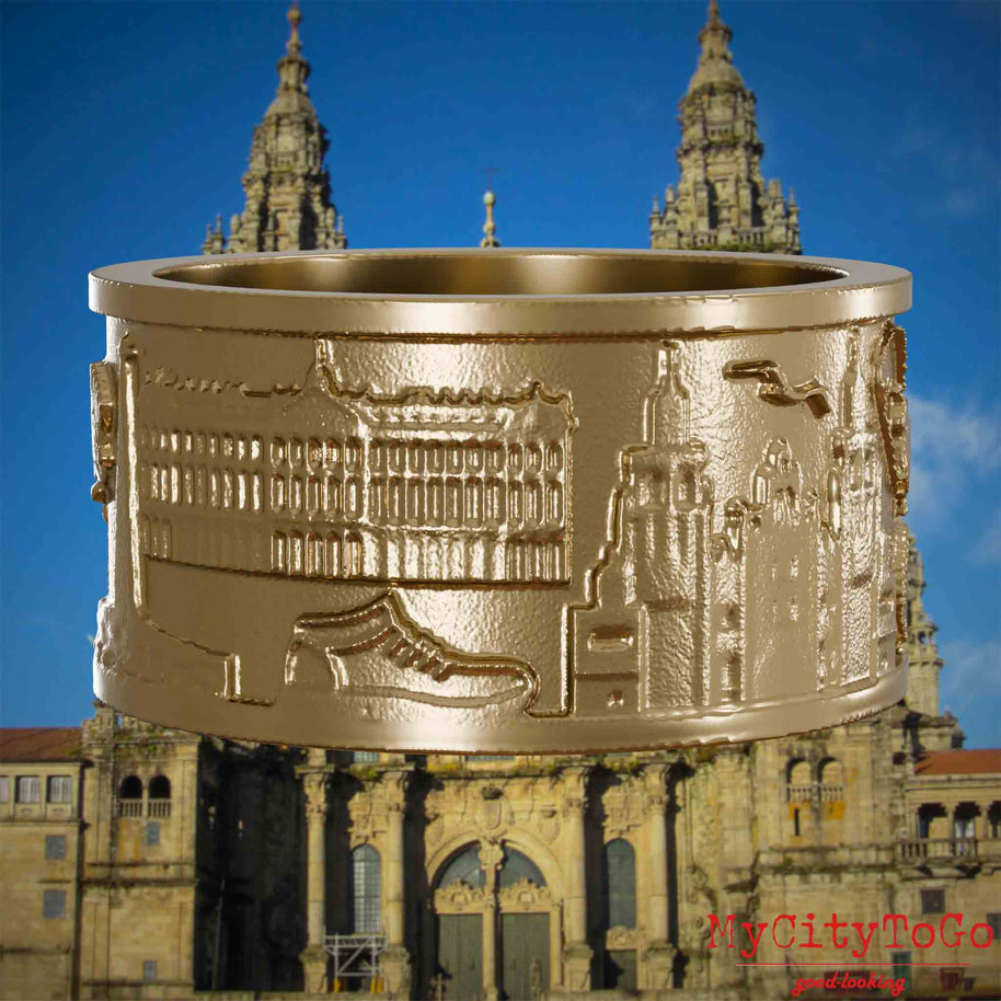 Ring aus vergoldetem Edelstahl mit Reliefs bekannter Sehenswürdigkeiten und Wahrzeichen auf dem Jakobsweg. Den Hintergrund bildet die Kathedrale von Santiago de Compostela.